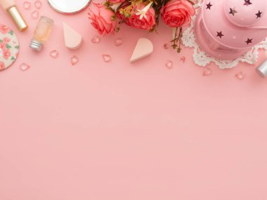 Kadın moda güzellik blogcusu çalışma alanı. Makyaj malzemeleri kozmetik, vücut jeli şişesi, tırnak cilası, pudra pudrası, aynalar, arka planda pembe kağıt üzerinde izole edilmiş gül çiçekleri fotokopi alanı. Üst görünüm