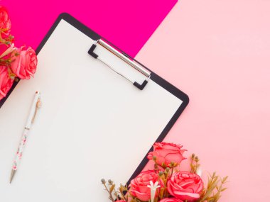 Ofis masasında pano, kalem ve etrafındaki çiçekler iki renkli arka plan pembesi ve morla izole edilmiş. Kadın yazar, fikirler, notlar, hedefler veya planlama konsepti. Üst manzara, düz uzanma.