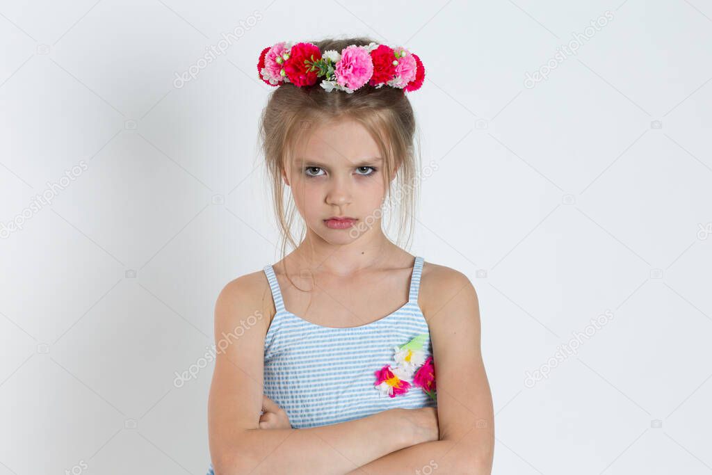 Sad upset girl kid looking at camera with arms crossed, folded hands. Closeup portrait of Caucasian kid model with floral headband isolated on white grey gray copy space background. Horizontal image.