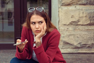 Üzgün kız cep telefonundan ya da erkek arkadaşından mesaj bekliyor. Dışarıdaki bir bankta oturuyor. Şehir dışından bir grupla.