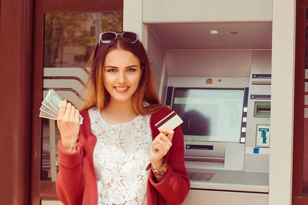 Withdraw. Happy Woman Holding Credit Card and money near ATM smiling looking at you camera happy. Summer, sunglasses on head casual clothing burgundy jacket white lace shirt, indian girl mixed race