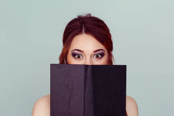 Shocked by the story. Young woman with shock wide eyed half face covered with brown black book