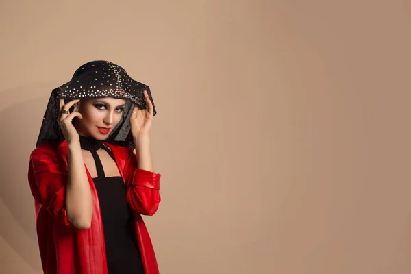 Arabic Beauty Arabic woman in red jacket looking at you smiling raising taking off her black hood decorated with crystals isolated on  brown background