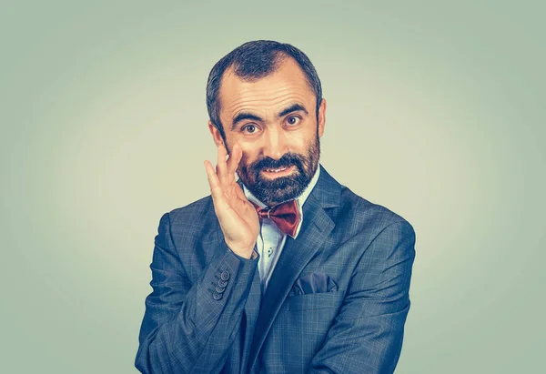 Business man whispering a gossip secret or confident personal information looking at camera telling you about a great deal. Mixed race bearded model isolated on light green studio copyspace background