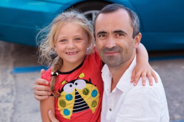 Mutlu, sevecen Amerikalı baba arka planda küçük kızı mavi arabayı kucaklıyor. Babalar gününde kaynaşmak, seyahat konseptine gitmek, gülümseyen tatlı kız babaya sarılmak..