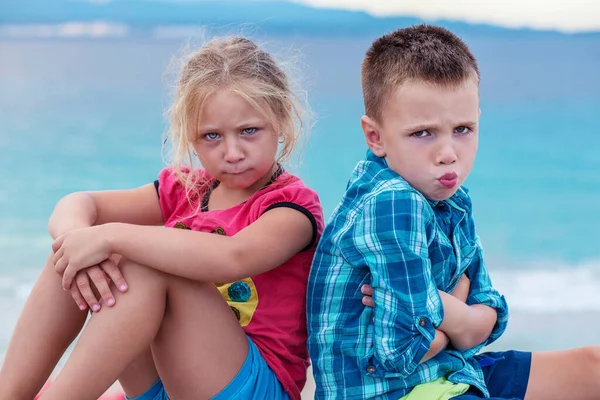 Upset siblings boy and girl sulking sitting with arms crossed back to back, not talking, kids brother sister ignoring each other after fighting sitting on the beach, children conflicts rivalry concept