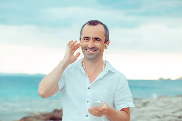 Man listening to music. Close up portrait smiling man guy listening to music looking at you camera by the sea hand year happy and enjoying nature music man. Happiness concept.