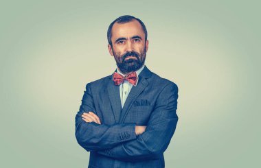 Koyu kahverengi saçlı, sakallı, iş adamı, mavi kravatlı ve beyaz düğmeli gömlekli. Kollarını kavuşturmuş mutlu patron açık yeşil arka planda izole edilmiş kameraya bakıyor.