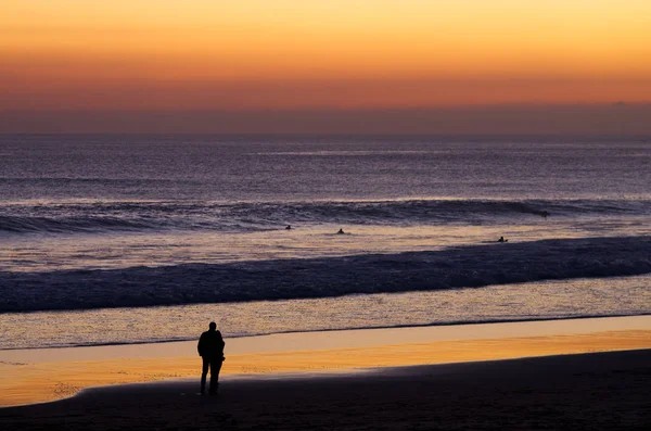 Coppia in spiaggia da crepuscolo guardando surfisti — Foto Stock