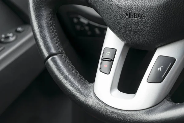 Hands free and media control buttons on the steering wheel in black leather, modern car interior