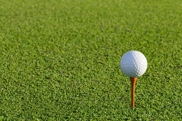 Bola de golfe no tee no campo de golfe sobre um verde turvo — Fotografia de Stock