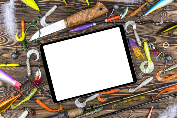 Fishing rod, tackles and fishing baits, reel on wooden board background with tablet computer isolated white screen, empty space for text