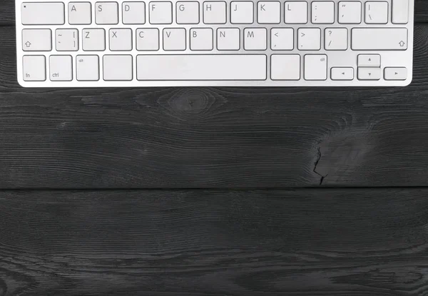 Vista cercana de un lugar de trabajo con teclado inalámbrico para computadora, teclas sobre fondo de mesa de madera negro viejo — Foto de Stock