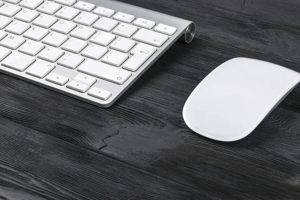 Vista de cerca de un lugar de trabajo de negocios con teclado inalámbrico de computadora, ratón y teclas sobre fondo de mesa de madera negro viejo — Foto de Stock