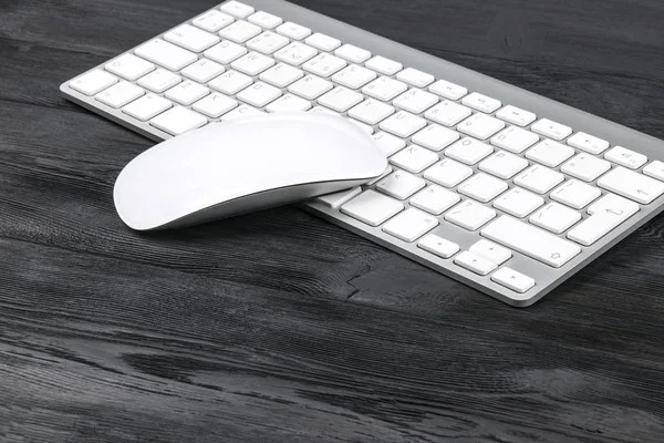 Vista de cerca de un lugar de trabajo de negocios con teclado inalámbrico de computadora, ratón y teclas sobre fondo de mesa de madera negro viejo — Foto de Stock