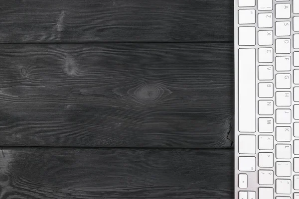 Vista de cerca de un lugar de trabajo de negocios con teclado inalámbrico de computadora, teclas en el fondo de mesa de madera negro viejo. Escritorio de oficina con espacio de copia — Foto de Stock