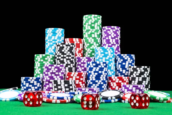 A set of poker chips stack on a green game table with a dice rolls. Black background. risk concept - playing poker in casino. Poker game theme. Red casino dice rolls.