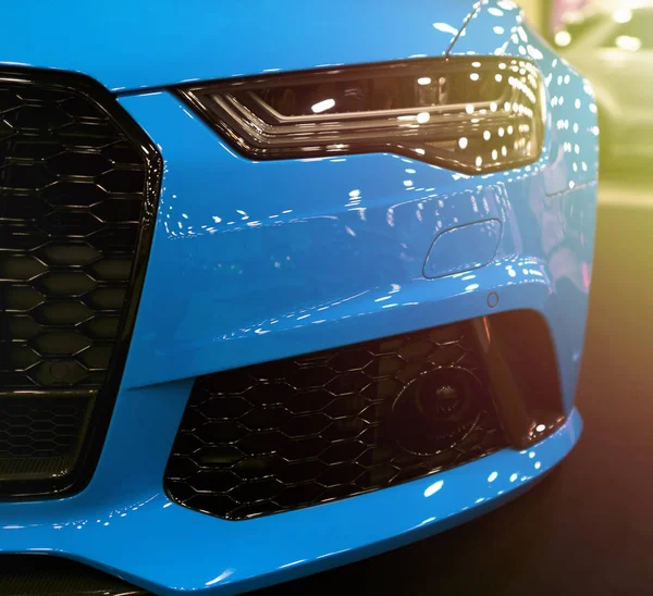 Vista frontal de azul moderno deporte de lujo con suave luz del sol naranja. Detalles exteriores del coche. Faro de un coche deportivo moderno. Las luces delanteras del coche —  Fotos de Stock