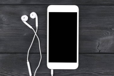 Siyah ahşap masa üzerinde kulaklık ile akıllı telefon. Smartphone ile izole perde. Metin için boş yer. Uzay kopyalayın. Smartphone boş ekran. Smartphone kadar sahte. kulaklık.