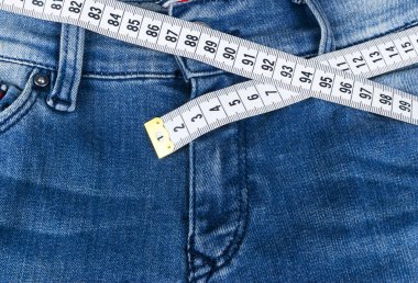 A mavi kadın kot pantolon ve cetvel, kavramı, diyet ve kilo kaybı. Teyp ölçme ile kot pantolon. Sağlıklı yaşam, diyet, fitness. Kilo kontrolü. Başarılı bir diyet. Fazla kilo azaltılması