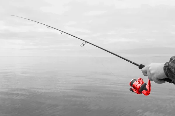 Manos de un pescador con una vara de hilar roja con la línea con una línea en un barco a motor en el lago en un día nublado —  Fotos de Stock