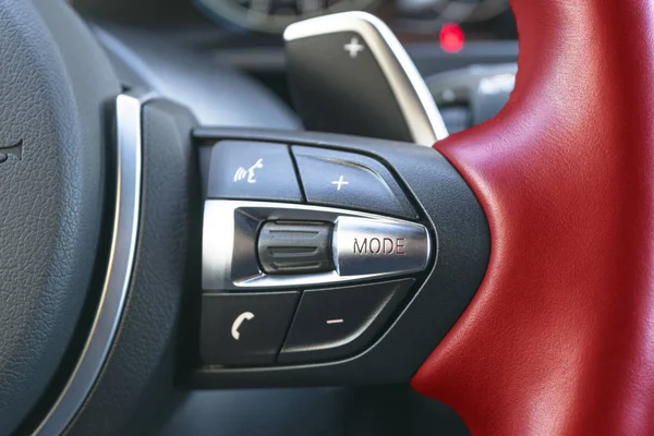 Hands free and media control buttons on the red steering wheel in black leather, modern car interior buttons on the steering wheel, modern car interior details