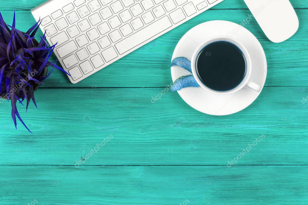 Office desk with copy space. Digital devices wireless keyboard and mouse on blue wooden table with cup of fresh coffee, top view