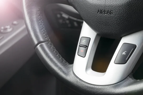 Hands free buttons on the steering wheel in black leather, modern car interior details. Soft lighting. Abstract view