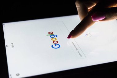Bir kadın eli tablet bilgisayar ipad Pro ekranda Google arama ana sayfasında arama için geceleri dokunuyor. En popüler Internet arama Google olduğunu
