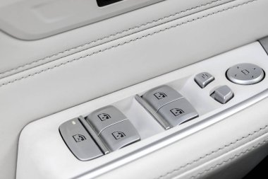 Lüks bir binek otomobilin güç pencere kontrol düğmeleri ile lüks bir passendoor kolu güç pencere kontrol düğmeleri ile kapı kolu. Dikiş ve doğal ahşap panel ile beyaz delikli deri iç. Modern araba iç detayları. Araba detaili