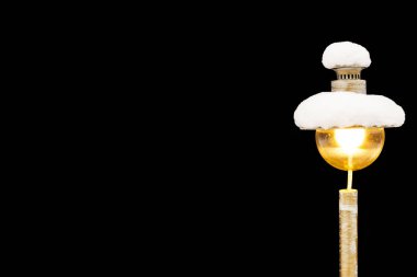 Karla kaplı bahçe lambası siyah arka planda izole edilmiş ve kırpma yolu var. Bir sokak lambası aydınlanır ve karla kaplanır..