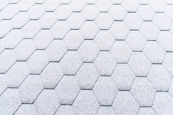 Asphalt roofing shingles texture covered with light snow. House roof shingles covered with frost. Snow covered roof of the house.