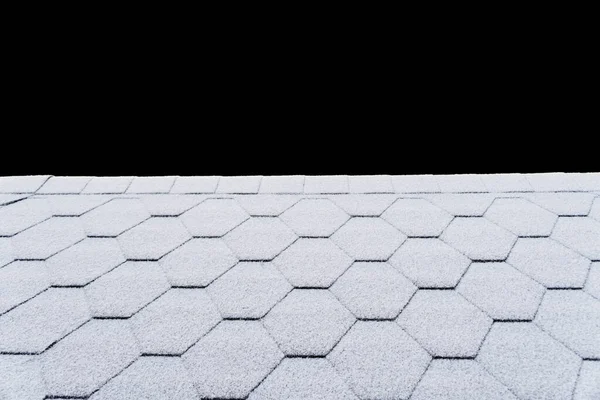 Asphalt roofing shingles texture covered with light snow. House roof shingles covered with frost. Snow covered roof of the house isolated on black background with clipping path.
