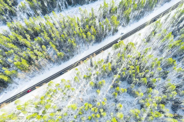 Aerial view of a winter country road in the forest with moving cars. Beautiful landscape. Captured from above with a drone. Aerial bird\'s eye road with car. Aerial top view forest. Texture of forest