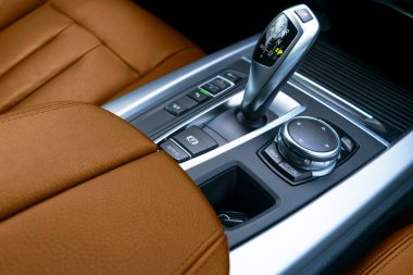Modern bir arabanın otomatik vites kolu (şanzımanı). Çoklu ortam ve navigasyon kontrol düğmeleri. Arabanın iç detayları. Şanzıman değişimi. İçi kahverengi deri..
