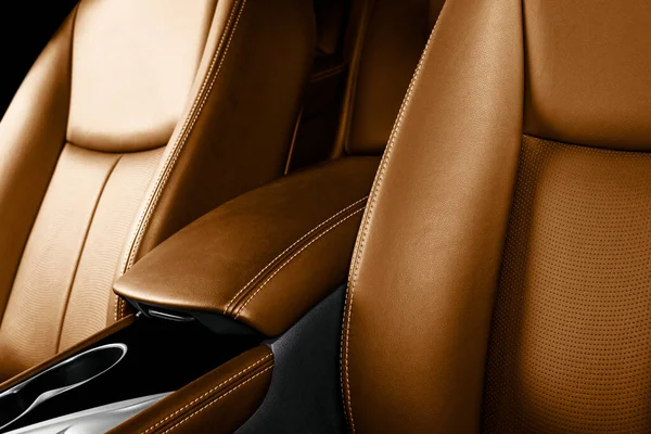 Brown leather interior of the luxury modern car. Perforated brown leather comfortable seats with stitching isolated on black background. Modern car interior details. Car detailing. Car inside