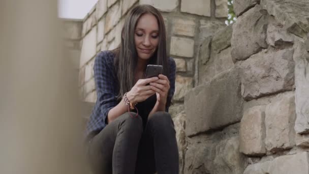 Hermosas mujeres jóvenes utilizan el teléfono móvil en tiempo feliz al aire libre dentro de la pared de ladrillo — Vídeos de Stock