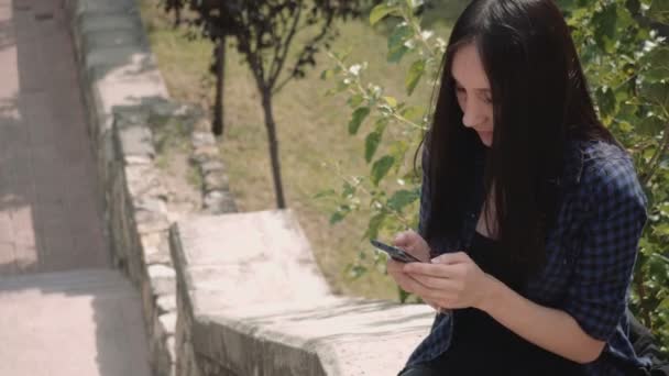 Portrét přitažlivou mladou ženou SMS na chytrém telefonu ve městě během slunečného dne — Stock video