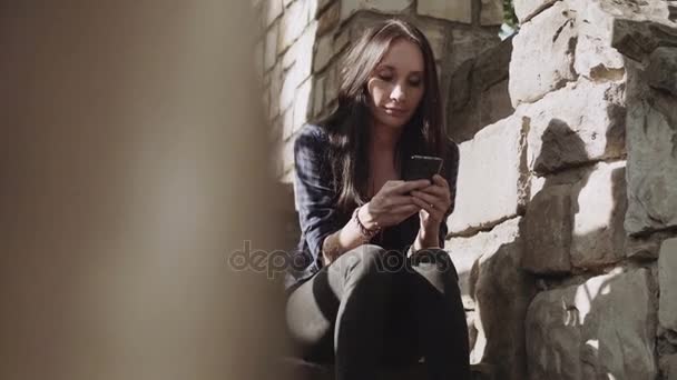 Belles jeunes femmes utilise le téléphone portable tout en étant assis sur les escaliers pendant le coucher du soleil — Video