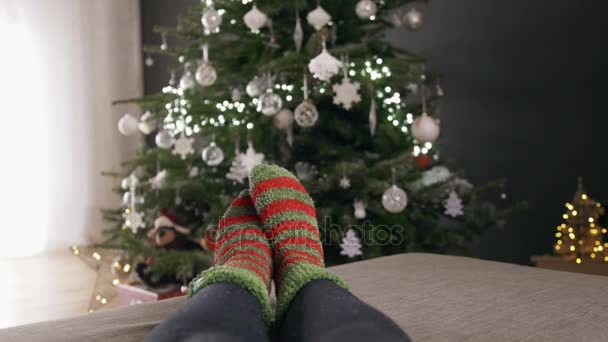 Pies de mujer en calcetines junto al árbol de Navidad, desenfoque árbol de Navidad en el fondo — Vídeos de Stock