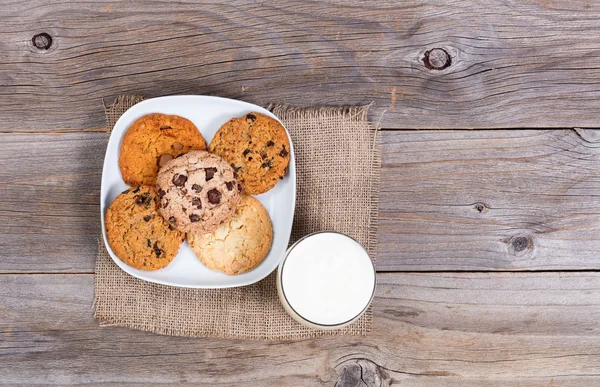 Variety of baked cookies in napkin and glass of milk on rustic w — Stock Photo, Image