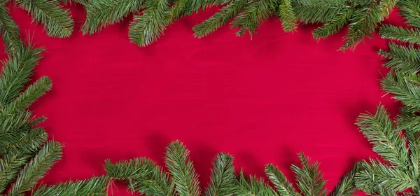 Evergreen branches forming border on red cloth — Stock Photo, Image