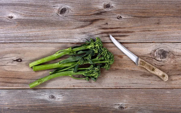 Fresh Chinese broccoli and paring knife on rustic wood — Stock Photo, Image