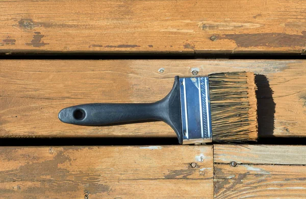 Used paintbrush filled with wood stain on a natural cedar deck — Stock Photo, Image
