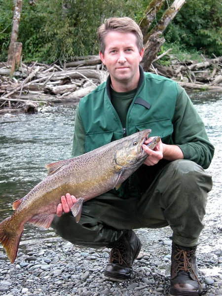 Visser bedrijf grote zalm vissen met rivier en bossen in de rug — Stockfoto