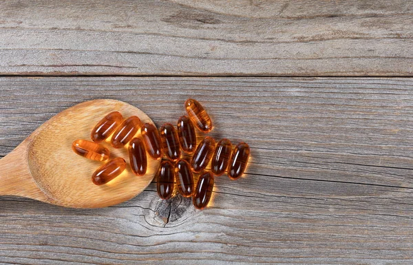 Organic pacific salmon fish oil capsules in wooden spoon on rust — Stock Photo, Image