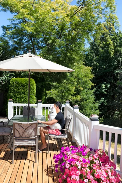 Young man with his dog working from home on his cedar deck — Stock Photo, Image