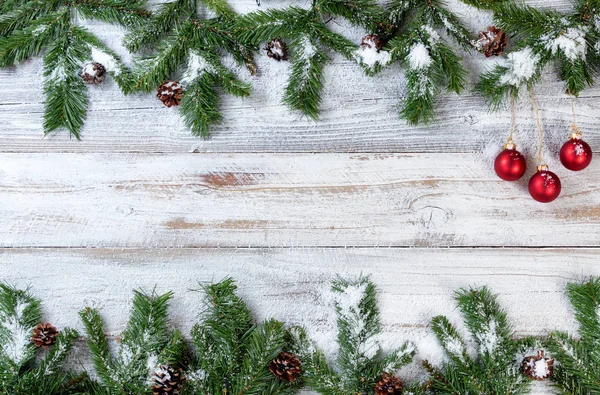 Snowy Christmas branches with red ornaments on rustic white wood — Stock Photo, Image