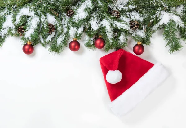 Rami di Natale innevati con cappello di Babbo Natale e ornamenti rossi — Foto Stock