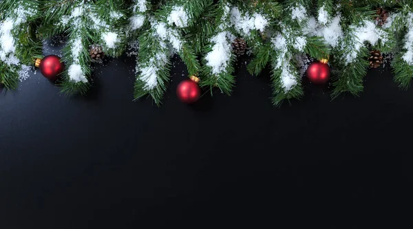 Снежные рождественские ветви с красными орнаментами на черном фоне — стоковое фото